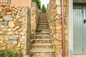 Un escalier en pierre menant à une porte, le tout entouré de murs de pierre et de verdure.