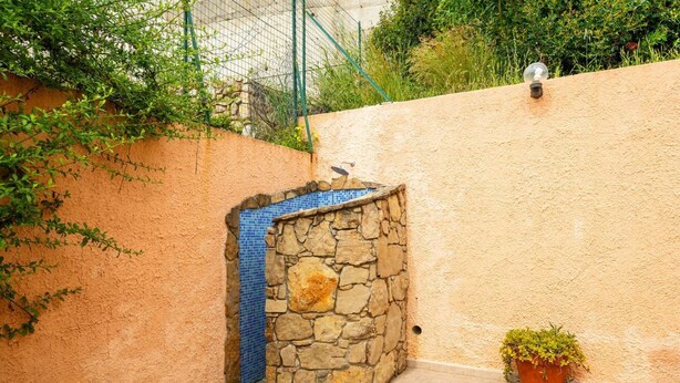 Un mur de pierres avec une section recouverte de carreaux, un pot de fleurs et une clôture en métal.
