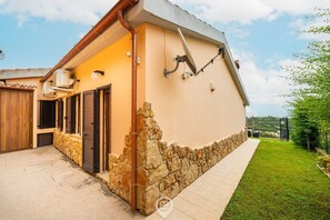 A two-story house with a stone foundation, a tiled patio, and a small garden.
