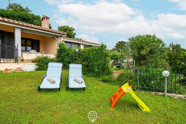 A house with a garden, two lounge chairs, and a swing set.