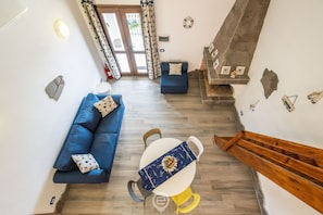 A modern living room with a blue sofa, a dining table with a blue tablecloth, and a staircase with a wooden handrail.