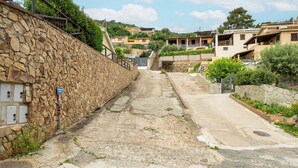 Un estrecho callejón con muros de piedra, un camino empedrado y edificios residenciales al fondo.