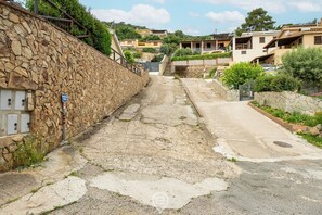 A narrow street with stone walls, a paved path, and residential buildings in the background.