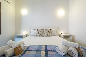 Un lit bien fait, recouvert d’une couvre-lit à carreaux bleus et blancs, avec deux oreillers assortis et deux lampes de chevet.