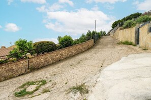 Un escalier en pierre menant vers le haut, avec une rampe métallique, entouré de verdure et sous un ciel dégagé.