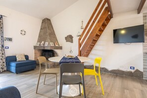 Un salon avec une cheminée en pierre, un canapé bleu, une table à manger avec des chaises, un fauteuil jaune et un téléviseur fixé au mur.