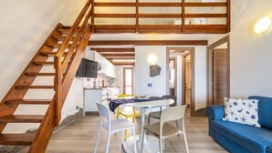 Un vaste espace de vie agrémenté d’un escalier en bois, d’une table à manger avec des chaises, d’un canapé et d’une cuisine en arrière-plan.