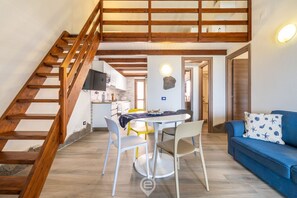 Un vaste espace de vie agrémenté d’un escalier en bois, d’une table à manger avec des chaises, d’un canapé et d’une cuisine en arrière-plan.