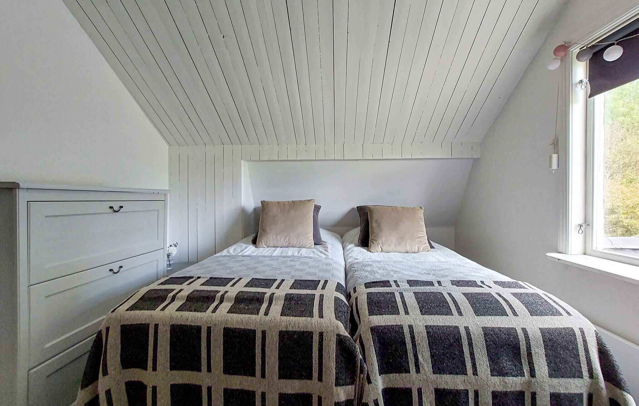 A bedroom with two beds, a window with curtains, and a white wardrobe.