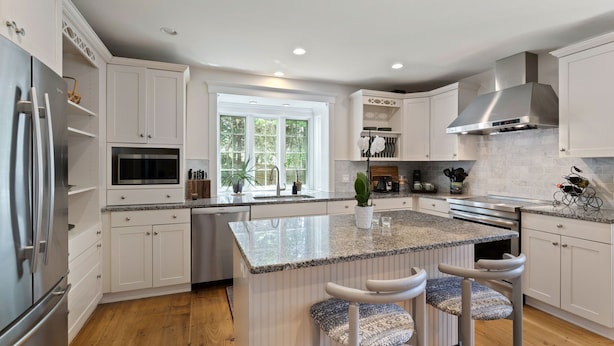 A modern kitchen with white cabinetry, a granite countertop, and a large window providing natural light.