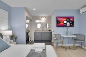 A modern hotel room with a bed, bedside table, TV, and a seating area with a table and chairs. - The Blue Gem - BRAND NEW ! (West Covina)