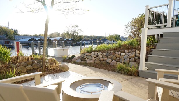A deck area with outdoor seating, a fire pit, and a view of a marina with boats. - The Harbor Hideout - Riverside home near Beaches, Pier, downtown shops (St. Joseph)