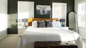 A bedroom with a large bed, a headboard, bedside tables, a lamp, and a wall-mounted artwork of a cow. - The Harbor Hideout - Riverside home near Beaches, Pier, downtown shops (St. Joseph)