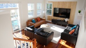 A spacious living room with a large TV, multiple seating areas, and large windows. - The Harbor Hideout - Riverside home near Beaches, Pier, downtown shops (St. Joseph)