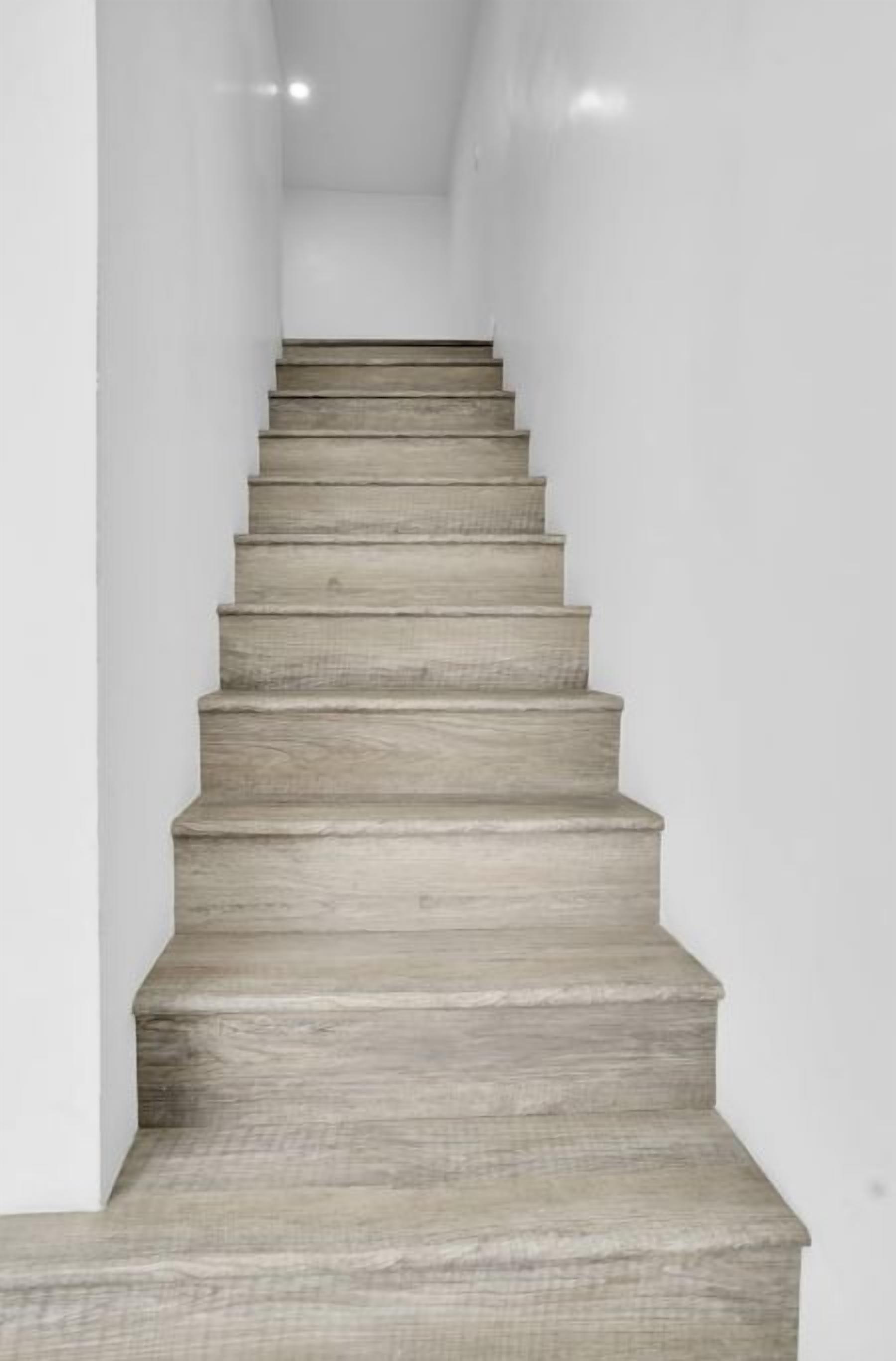 Una escalera con acabado en madera clara que sube por un pasillo estrecho con paredes blancas.