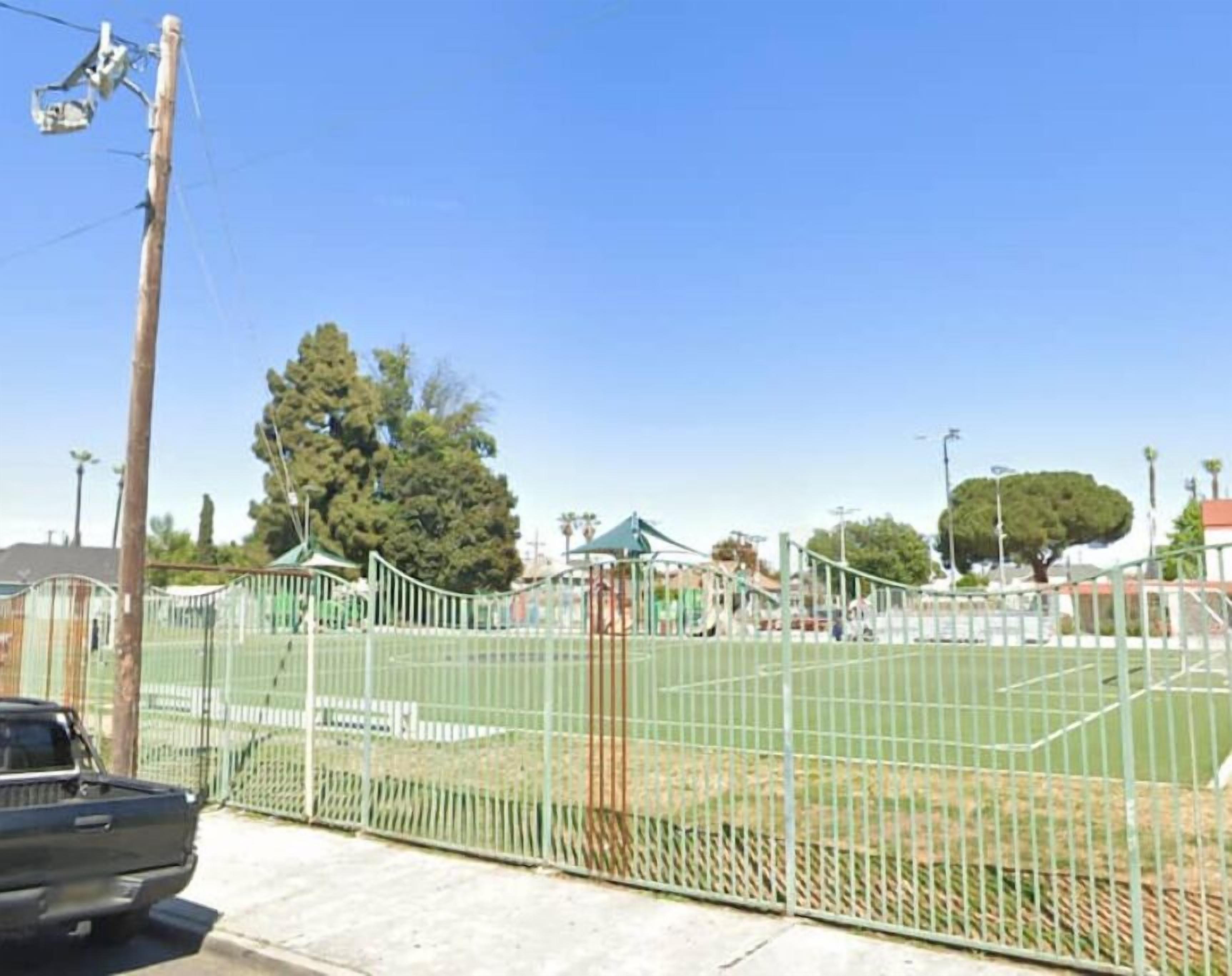 A fenced sports field with a playground and a green-roofed building in the background.