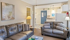 Ein Wohnzimmer mit zwei Ledersofas, einem Deckenventilator, einem Gemälde und einer Küche im Hintergrund.