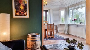 Una stanza accogliente con una parete verde scuro, una botte di legno, un quadro incorniciato e vista su una sala da pranzo attraverso una finestra.