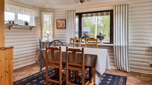 Zona pranzo con tavolo e sedie in legno, un lampadario e ampie finestre con tende.