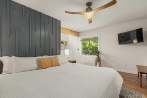 A bedroom with a bed, a ceiling fan, a TV, a window, and a plant. - Cozy Cottage | 2 min to WNC AG Center | Pet Friendly (Fletcher)
