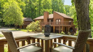A wooden deck with wicker chairs and a table, overlooking a building with a balcony. - Cozy Cottage 2 min to WNC AG Center Pet Friendly (Fletcher)