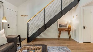 A modern living room with a black staircase, a wooden coffee table, a sofa, and a lamp. - Cozy Cottage 2 min to WNC AG Center Pet Friendly (Fletcher)
