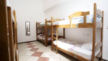 A dormitory room with bunk beds, numbered beds, a tiled floor, and a framed picture on the wall.