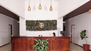A reception desk with a wooden finish, a large potted plant in the foreground, and a decorative wall with a giraffe head motif. - Ukinca Hostel (Bahía Ballena)