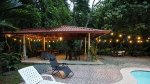 A covered outdoor seating area with string lights, a pool, and lounge chairs. - Ukinca Hostel (Bahía Ballena)