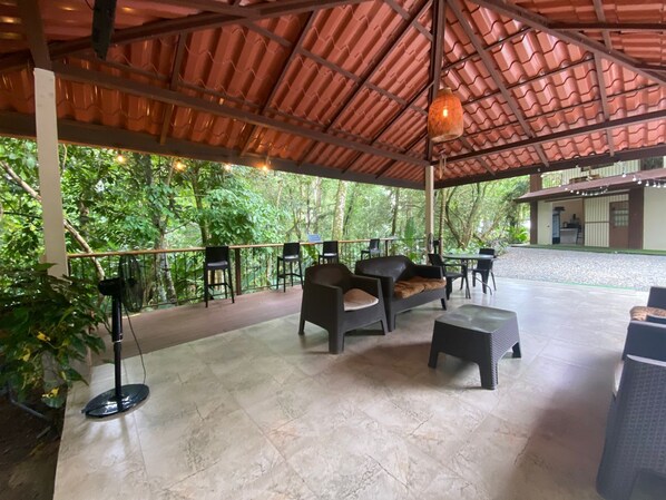 An outdoor covered patio with seating, a stage, and a view of lush greenery. - Ukinca Hostel (Bahía Ballena)