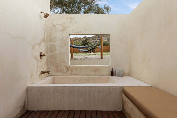 Una bañera con vista por la ventana a una hamaca y un poste de madera.