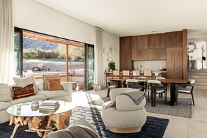 A modern living room with a glass coffee table, a sofa, and a dining area with a wooden table and chairs.