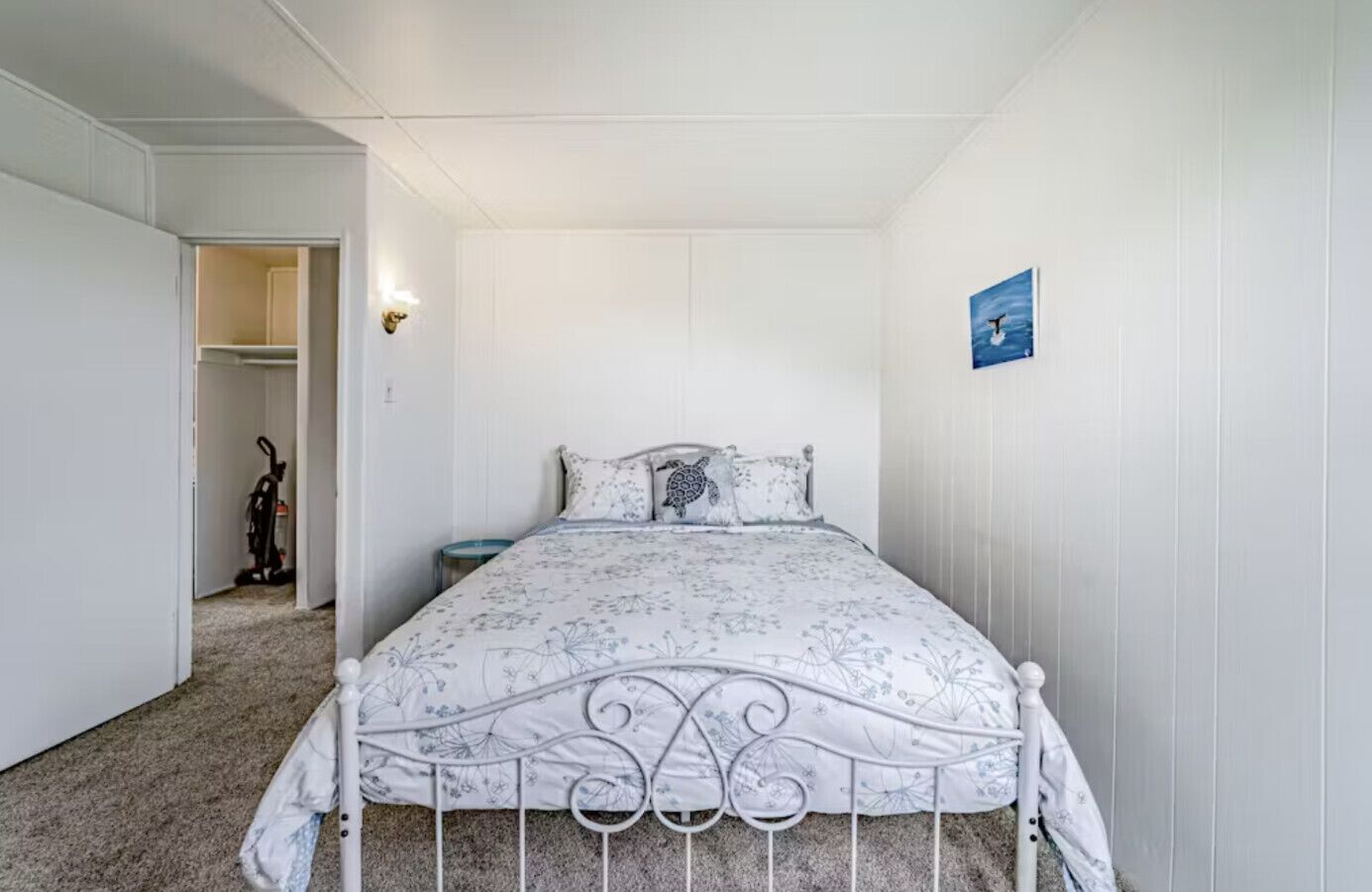 A bedroom with a bed, a nightstand, a wall-mounted light, and a painting.