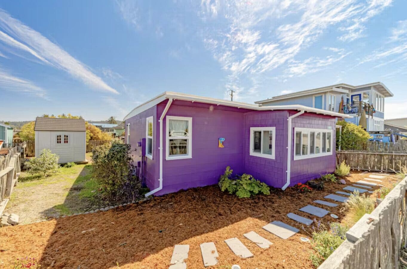 A purple single-story house with a small garden and a wooden deck.