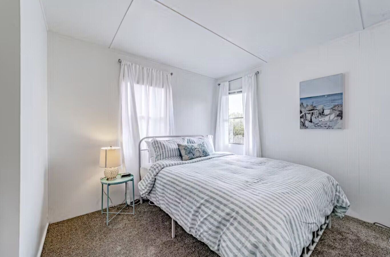 Une chambre à coucher avec un lit, une table de chevet, une lampe et une fenêtre avec des rideaux.
