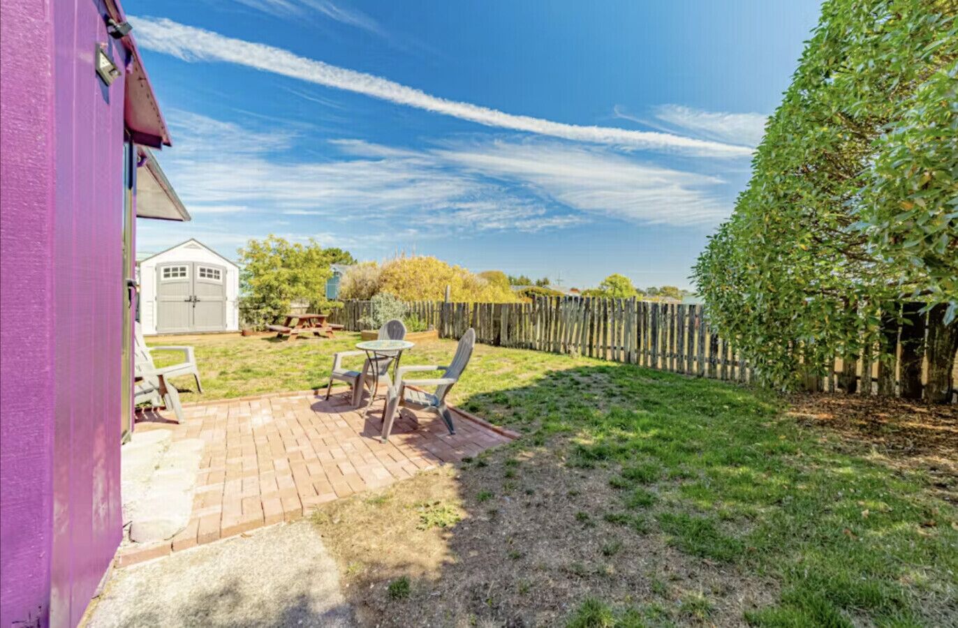A backyard with a patio, a shed, and a wooden fence.