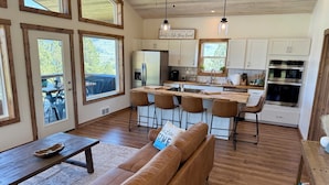 A spacious kitchen with wooden cabinets, a central island with bar stools, and a view of the outdoors through large windows. - Wild Horse Sunrise at Flathead Lake (Big Arm)