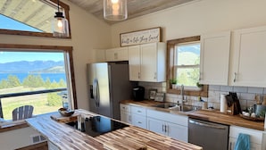 A modern kitchen with a large island, stainless steel appliances, white cabinets, and a view of the mountains. - Wild Horse Sunrise at Flathead Lake (Big Arm)