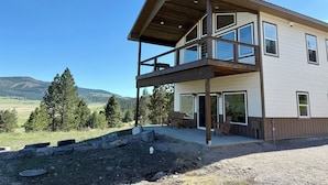 A two-story modern house with a balcony, large windows, and a view of a forested area. - Wild Horse Sunrise at Flathead Lake (Big Arm)
