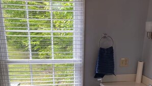 Ein Badezimmer mit großem Fenster, Holzboden, einem Waschbecken und dunklen Schränken.