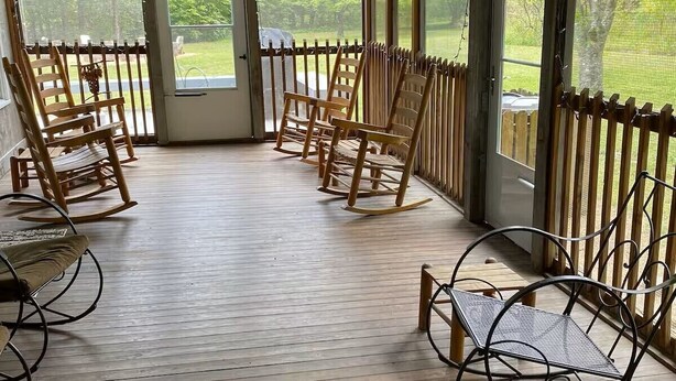 Eine überdachte Veranda mit Holzboden, Schaukelstühlen, einer Bank und einem Deckenventilator.