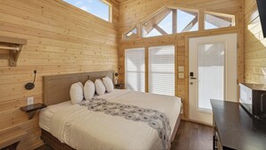 A wooden cabin room with a bed, a desk, and a large window.