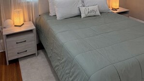 A bedroom with a bed, nightstands, a bedside lamp, and sheer curtains. - Cozy 4-bedroom house in South-Utica! (Utica)