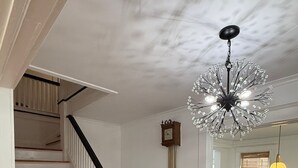 A staircase with white railings and wooden steps, a chandelier, a wall clock, and a dining area with a table and chairs. - Cozy 4-bedroom house in South-Utica! (Utica)