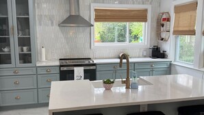 A modern kitchen with a large island, bar stools, and a view of greenery outside. - Cozy 4-bedroom house in South-Utica! (Utica)