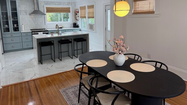 A modern kitchen with a central island, bar stools, and a dining table with placemats. - Cozy 4-bedroom house in South-Utica! (Utica)