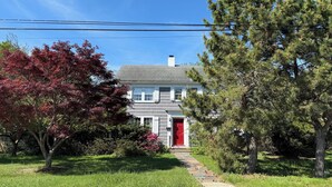 A two-story house with a red door and a stone pathway leading to it.