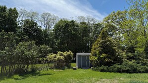 A small, single-story building with a flat roof, surrounded by lush greenery and trees.