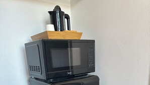 Et sort køleskab med en mikrobølgeovn ovenpå, placeret op ad en hvid væg.