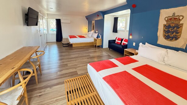 A hotel room with two beds, a wooden bench, a desk, and a television on the wall.